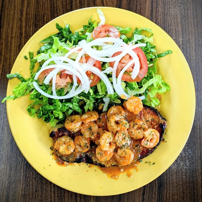Riva's Bbq Restaurant's grilled steak topped with shrimp and sauce, served with a fresh salad.