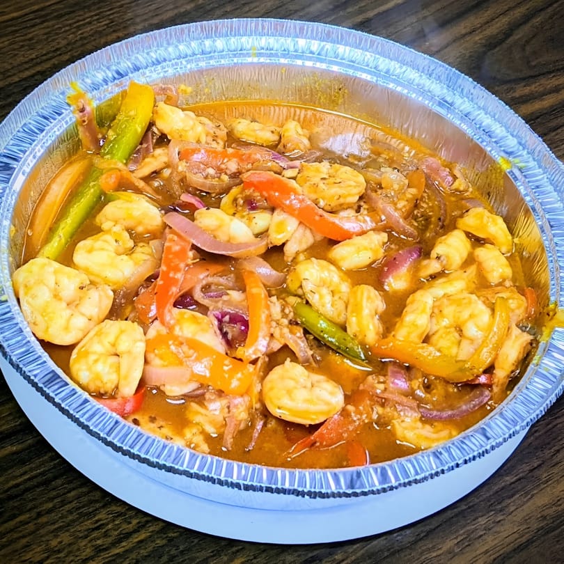 Shrimp and vegetables in a rich sauce, served in a foil takeout container from Riva's BBQ.